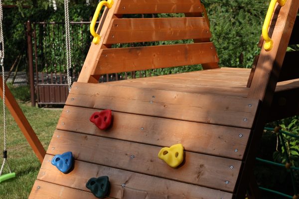 Wooden playground set with climbing wall, rope net, and two swings for kids, designed for safe and active outdoor play